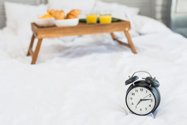 Tasty food on breakfast table and alarm clock on bed