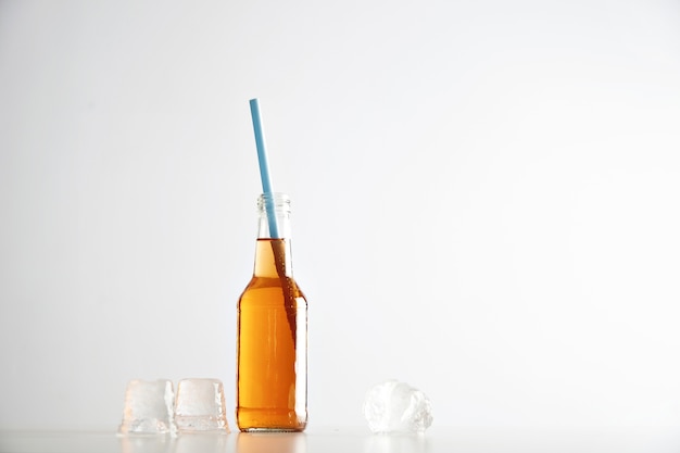 Tasty fresh cocktail in transparent bottle with blue drinking straw near ice cubes isolated on white