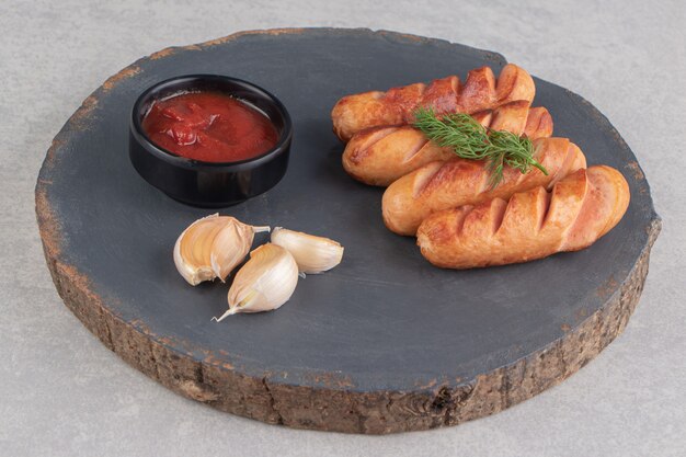 Tasty fried sausages, garlic and ketchup on wood piece.