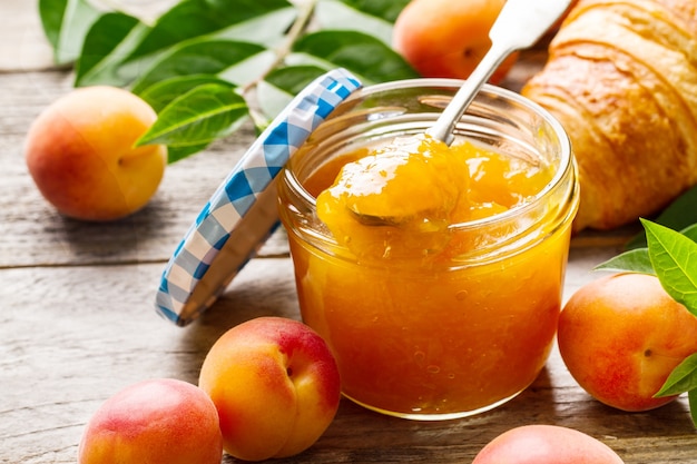 Tasty fruit orange apricot jam in glass jar with fruits on wooden table. Closeup. 