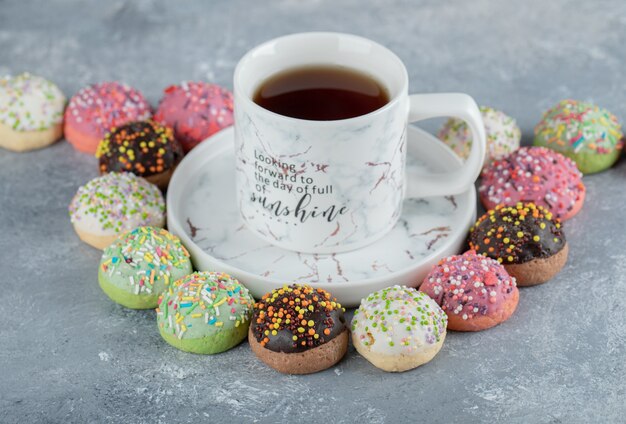 Tasty glazed cookies around cup of tea.