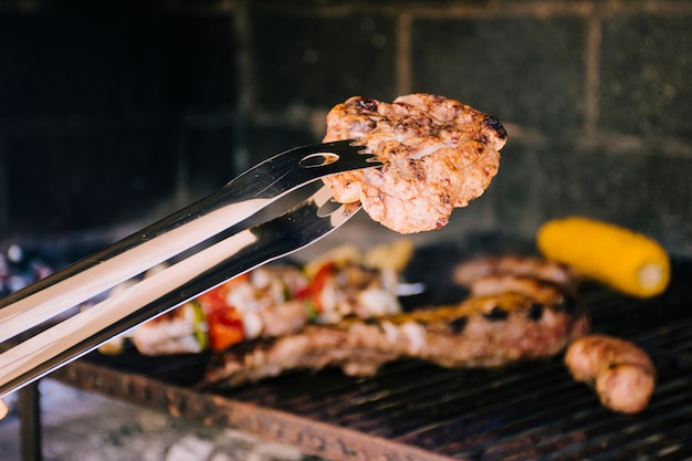 Tasty grilled piece of meat in metal tongs