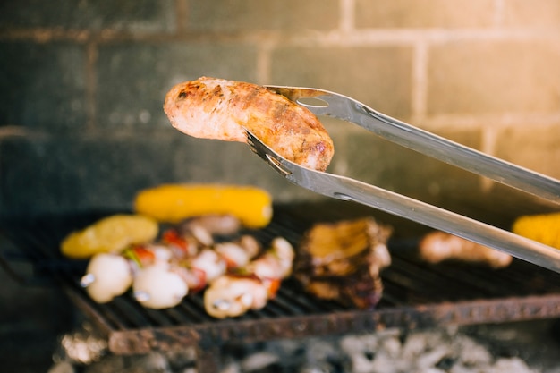 Tasty grilled sausage in metal tongs