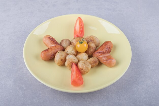 Tasty grilled sausages and potatoes on yellow plate. 