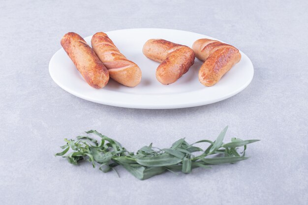 Вкусные сосиски на гриле на белой тарелке.
