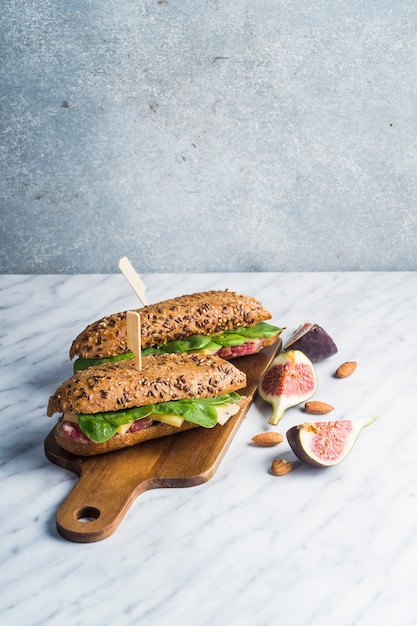 Tasty hot dogs on chopping board with fig and almonds over white marble counter