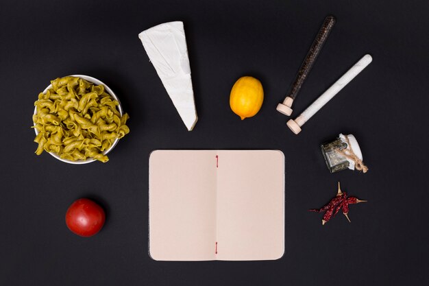 Tasty ingredient for making pasta with open blank diary on black surface