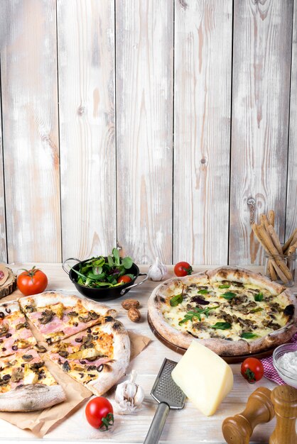 Вкусная итальянская пицца со свежими ингредиентами и посудой перед деревянной стеной