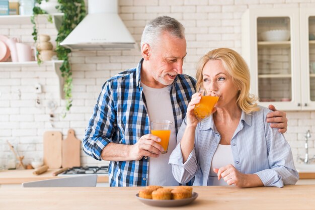 Tasty muffins in the front of smiling senior man looking at her wife drinking the juice