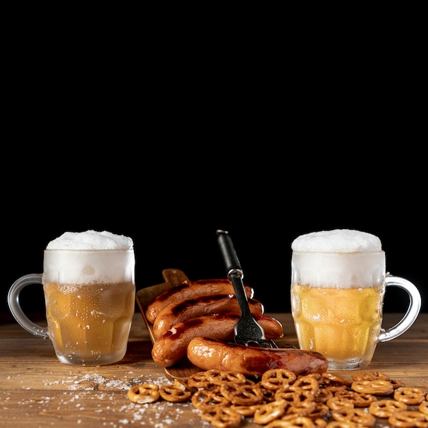 Tasty mugs of beer with sausages on a table