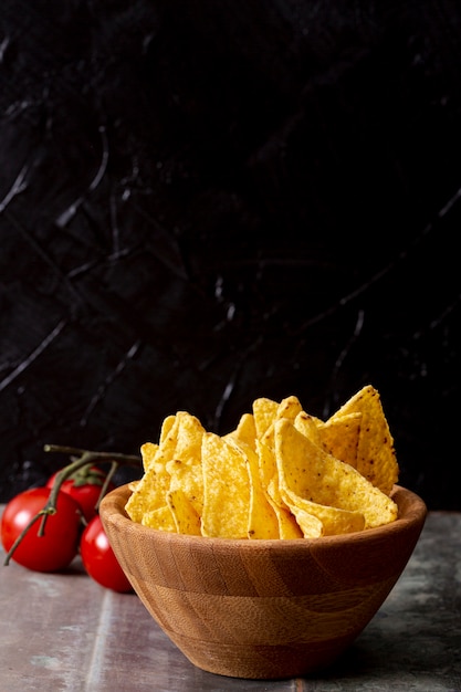 Tasty nachos in wooden bowl and tomatoes