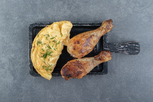 Tasty omelette and chicken legs on black board.