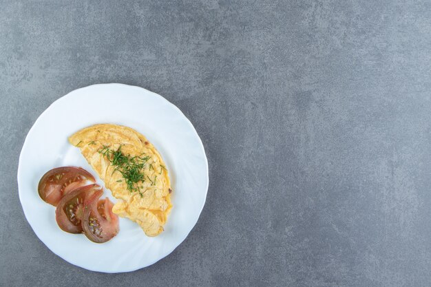 Tasty omelette and tomato slices on white plate