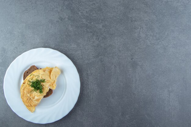 Tasty omelette with bread on white plate.