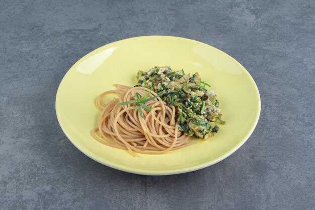 Tasty omelette with greens and spaghetti on yellow plate.