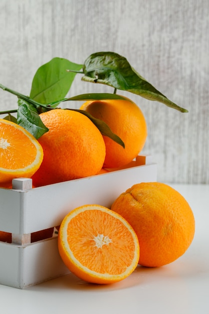 Tasty oranges in a wooden box with branch and slices side view