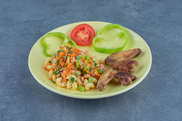 Tasty pasta and chicken wings on yellow plate.