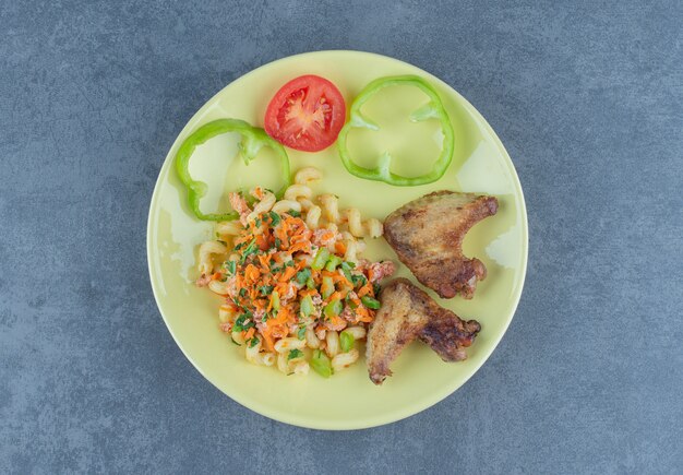 Tasty pasta and chicken wings on yellow plate.