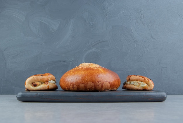 Tasty pastries with cheese and bun on black board.