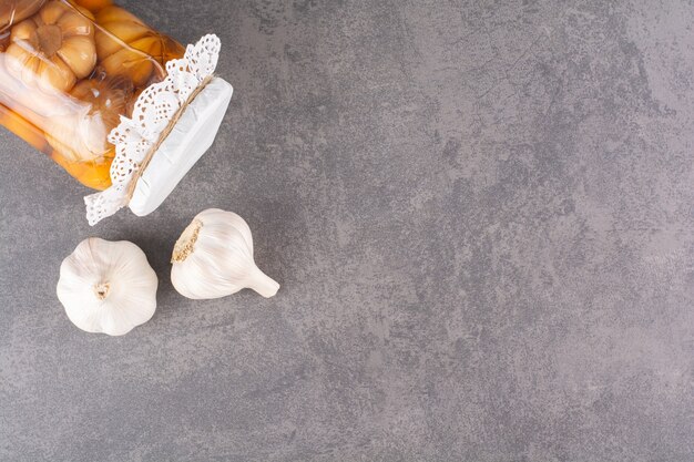 Tasty pickled garlic in glass jar placed on stone table.