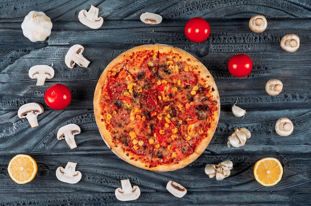 어두운 나무 배경에 토마토, 레몬, 마늘, 버섯 평면도와 맛있는 피자