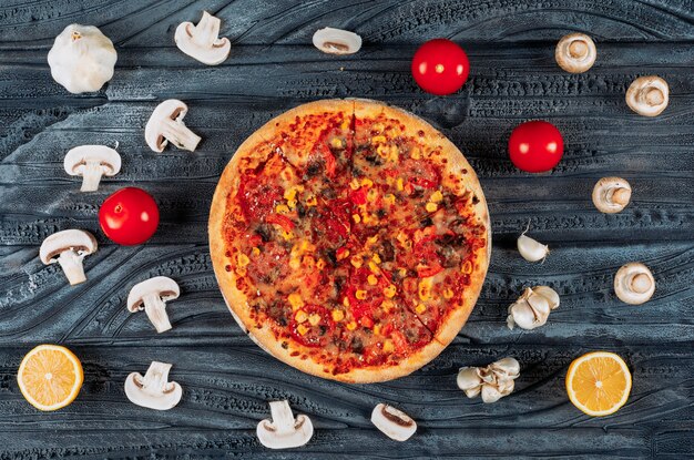 暗い木製の背景にトマト、レモン、ニンニク、キノコの上面とおいしいピザ