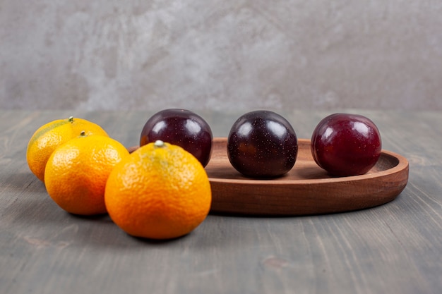 Tasty plums with delicious tangerines on a wooden plate. High quality photo