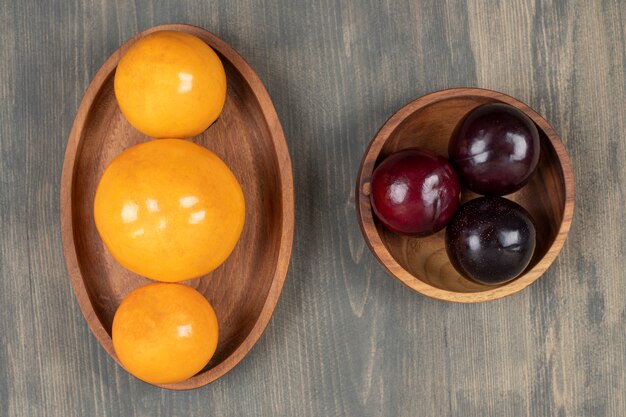 Tasty plums with delicious tangerines on a wooden plate