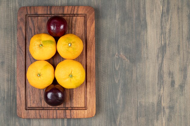 Free photo tasty plums with delicious tangerines on a wooden plate