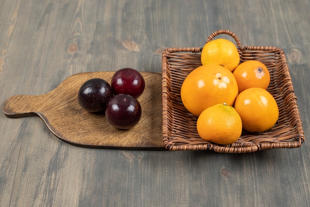 Free photo tasty plums with delicious tangerines on a wooden plate