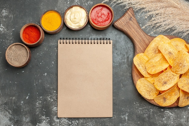 Tasty potato chips spices with ketchup and notebook on gray background