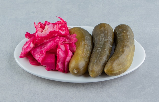 Tasty red sauerkraut and cucumber on a plate on the marble surface