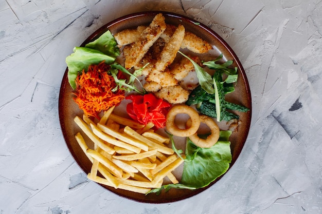 Foto gratuita gustosi antipasti da ristorante per grandi aziende tra cui pepite di pollo dorate patate fritte insalata verde foglie e cetrioli freschi in piedi su un tavolo bianco