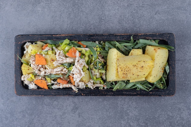 Tasty salad and boiled potatoes on black plate.