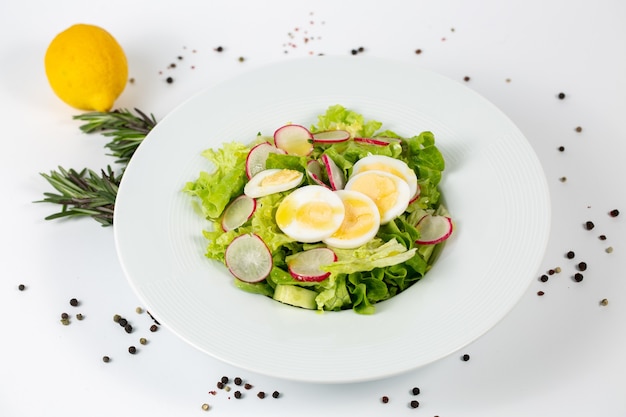 Вкусный салат с листьями салата, редисом и яйцом на белом