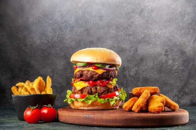 Tasty sandwich and chicken nuggets on brown wooden cutting board fries on dark ice surface