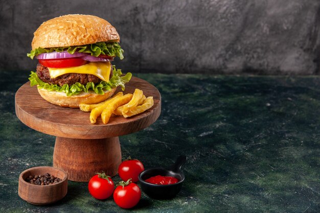 Вкусный сэндвич-фри на деревянной разделочной доске, помидоры, кетчуп на темной поверхности смешанного цвета со свободным пространством