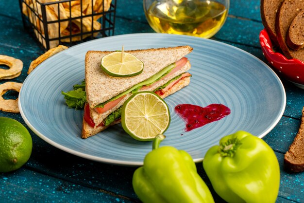 tasty sandwich inside blue plate along with green bell-peppers and oil on blue
