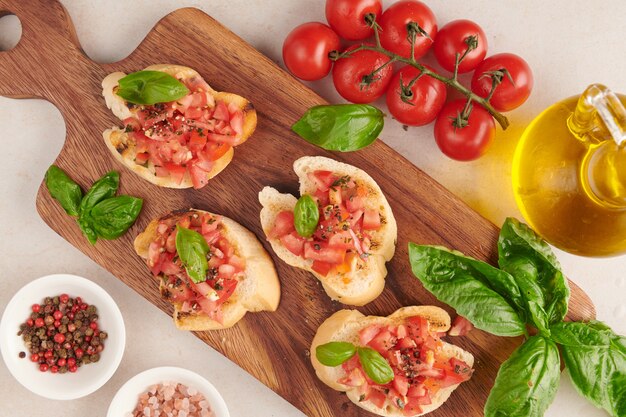 Tasty savory tomato Italian appetizers, or bruschetta, on slices of toasted baguette garnished with basil, vegetables, herbs on grilled or toasted crusty ciabatta bread.
