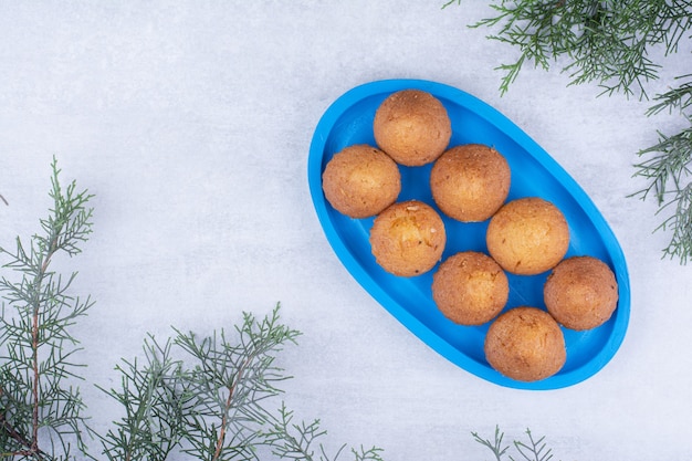 Tasty small cakes on blue plate with pine branch.