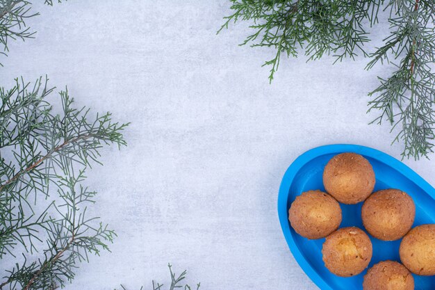 Tasty small cakes on blue plate with pine branch