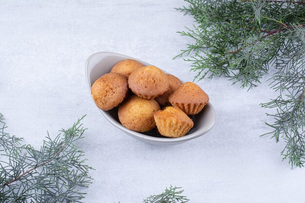 Tasty small cakes in ceramic bowl with pine branch.