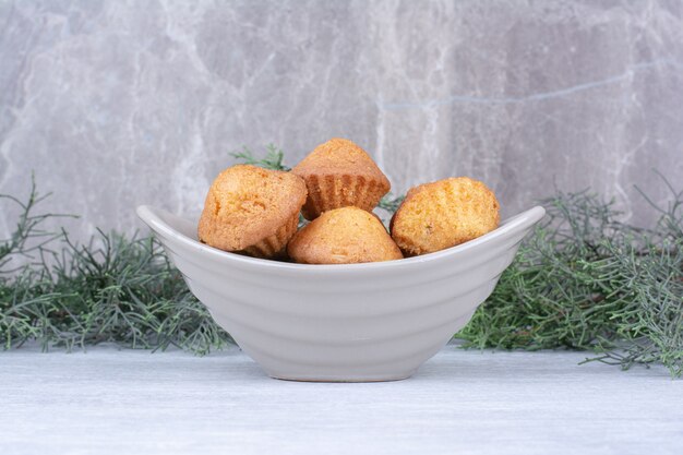 Tasty small cakes in ceramic bowl with pine branch