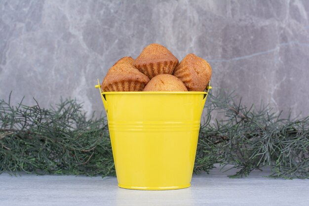 Tasty small cakes in yellow bucket with pine branch.