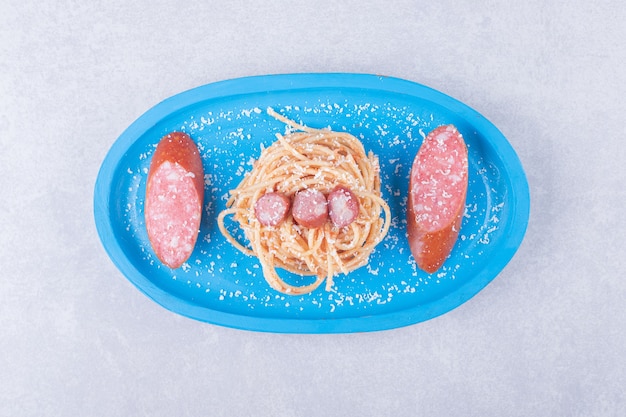 Tasty spaghetti with sausages on blue plate.