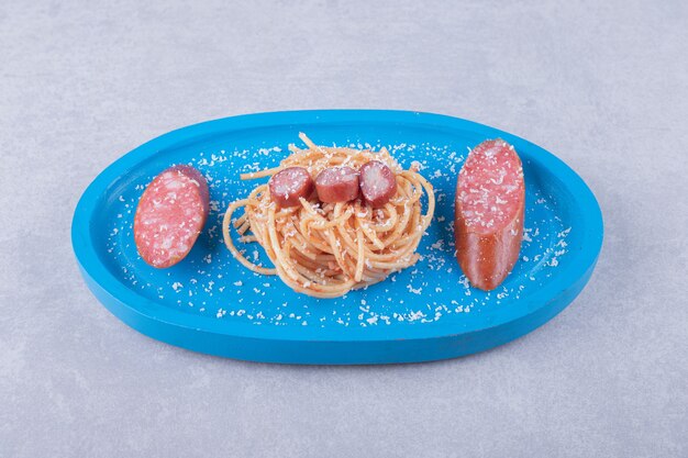 Tasty spaghetti with sausages on blue plate.