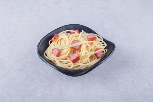 Tasty spaghetti with sliced sausages in black bowl.