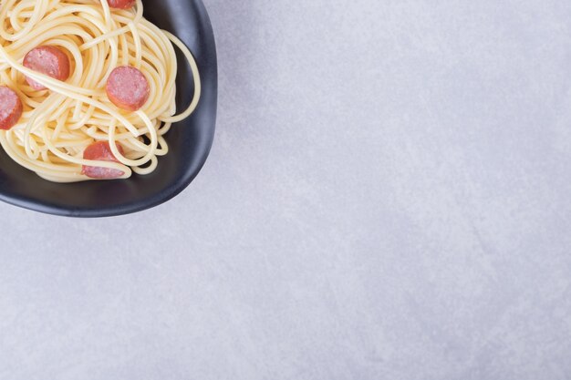 Tasty spaghetti with sliced sausages in black bowl. 