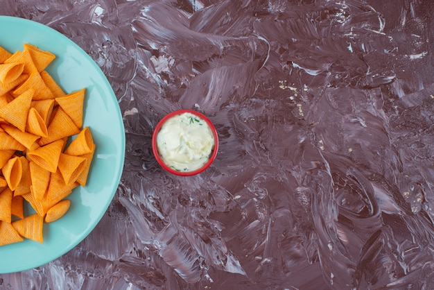 Tasty spicy chips on a plate next to yogurt on the marble surface