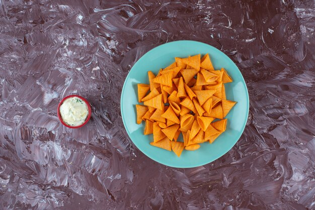 Tasty spicy chips on a plate next to yogurt, on the marble table.